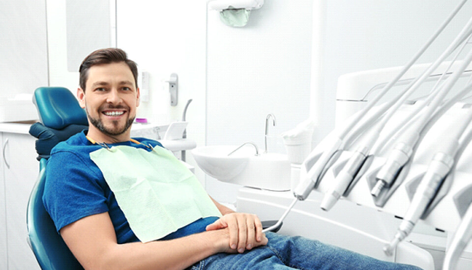 Man in blue shirt sitting in dental chair and smiling